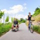 Young couple enjoying time outdoors. She is cycling, he is sitting in a wheelchair.